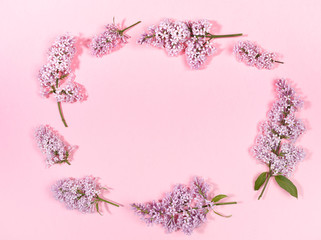 Creative floral spring background with twigs of lilac laid out in oval with copy space inside it on trendy pink background. Top view, flat lay.