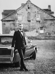 Elegant groom in bow-tie. Groom in a suit standing near retro car. black and white image