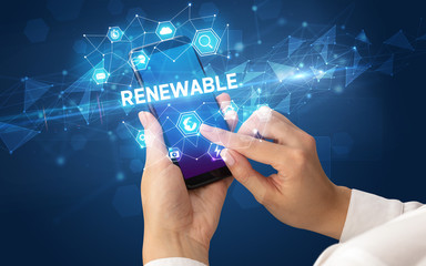 Female hand holding smartphone with RENEWABLE inscription, modern technology concept