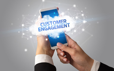 Female hand touching smartphone with CUSTOMER ENGAGEMENT inscription, cloud business concept