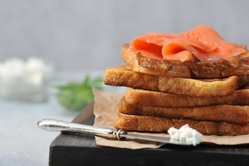 Slices of fried bread and slices of salmon with weak salt. Close-up. In the background is a cup of greens and soft cheese.