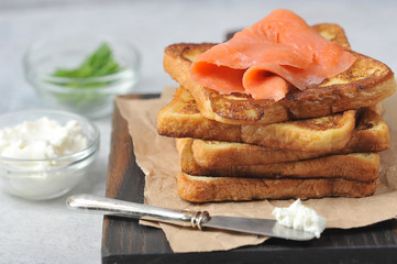 Slices of fried bread and slices of salmon with weak salt. Next to toast is a knife with soft cheese. Light background. Close-up. Macro shot.