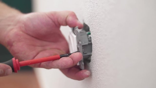 electrician installing electrical socket with screwdriver in wall