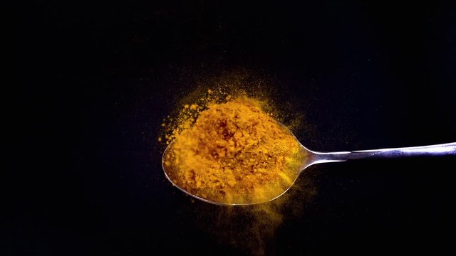 A Full Spoon Of exotic spice turmeric Flying up and Falling down on black background closeup in super slow Moti