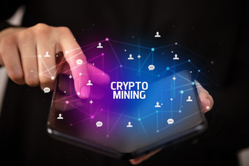 Businessman holding a foldable smartphone with CRYPTO MINING inscription, new technology concept
