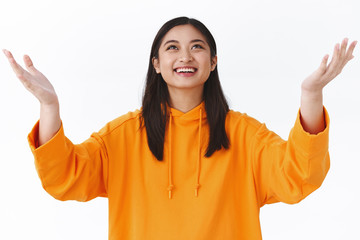 Girl catching something from sky. Cheerful happy asian woman raising hands up and smiling looking upwards at falling object, thanking god, feel relieved and delighted dream come true, accomplish goal