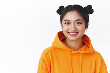 Close-up portrait friendly happy kawaii asian girl in orange hoodie with two cute hairbuns, smiling happy camera, show positive joyful emotions, standing white background, concept of beauty