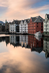 Fototapeta na wymiar A vertical sunset photograph of beautiful buildings reflecting off the water, taken in Aalesund, Norway.