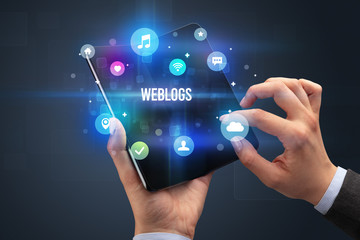 Businessman holding a foldable smartphone with WEBLOGS inscription, social media concept