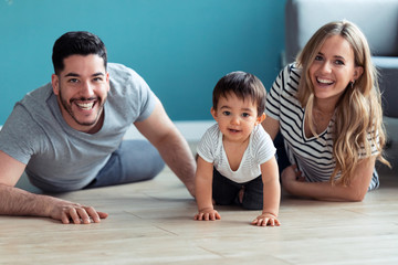 Pretty young parents looking at camera while playing with baby son at home.