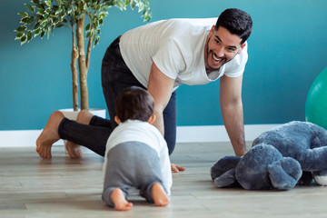 Smiling young father has fun with little baby while are crawling on the floor together at home.