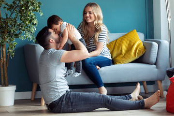 Pretty young parents playing with baby son while sitting on the floor at home.
