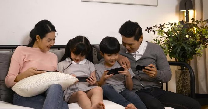 Happy asian family shopping or playing game online together. The father's mother and children sit on the couch enjoying smartphones together.
