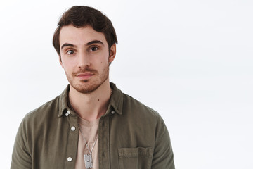 Obraz premium Close-up portrait of handsome macho man with beard in olive shirt, smile cheeky and looking camera with friendly, relaxed expression, standing joyfuly over white background, advertising