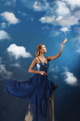 Fototapeta na wymiar girl on the ladder reaches up with her hands. A young woman in a blue dress on a blue background