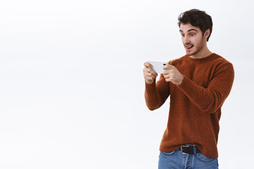 Enthusiastic good-looking caucasian guy in sweatshirt holding smartphone horizontally, showing tongue and looking display with interest and excitement, playing awesome game