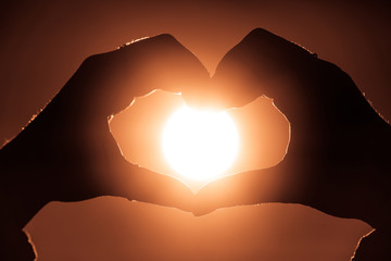 Female hands in heart shape in focus holding sun circle inside