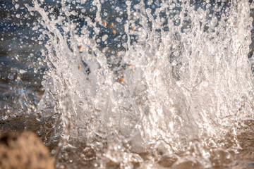 Water spray produced by wave on beachline, selective focus on water splashes