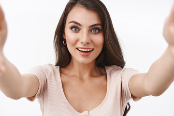 Fototapeta premium Connection, online and people concept. Waist-up shot lovely caucasian female looking curious and surprised, holding camera, taking selfie, record lifestyle, beauty video for vlog, white background