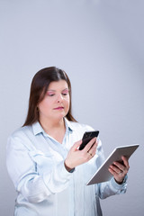 Business Woman Poses for a Studio Portrait. She is texting on her smartphone and reading information from a tablet.