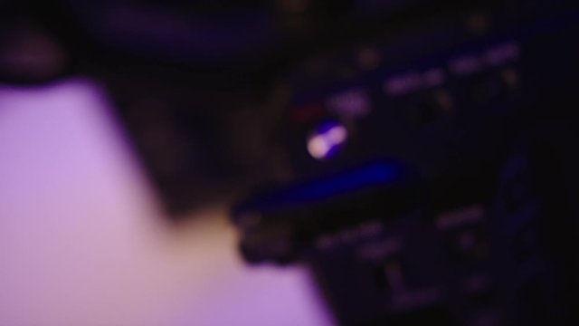 Sony camera: the top handle record button on an ENG video camera.. Close up studio shot on a white surface with neon blue/violet light. Rack focus