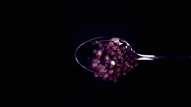 A Full Spoon Of falling peppercorns down on black background closeup in super slow motion