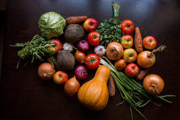 onions, garlic, tomato, greens, parsley, arugula, cabbage, apples, beetroot, carrots, pumpkin, lie on a wooden table