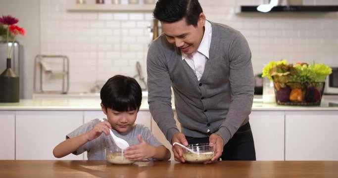 Little Asian Boy Eating Breakfast With Father. Father Preparing Meal For Son Enjoying Delicious Homemade Meal In Kitchen At Home Getting Ready For School.
