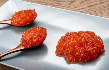 Red caviar in wooden spoons in a gray rectangular plate