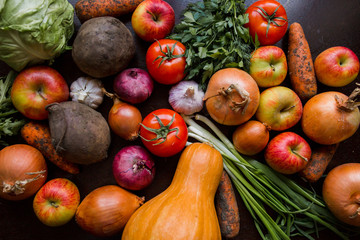 onions, garlic, tomato, greens, parsley, arugula, cabbage, apples, beetroot, carrots, pumpkin, lie on a wooden table