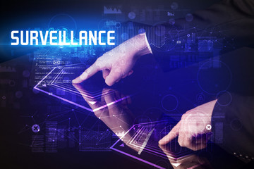 Hand touching digital table with SURVEILLANCE inscription, new age security concept