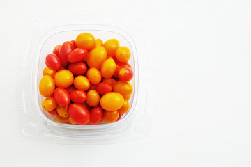 Red and yellow tomatoes in transparent box on white background