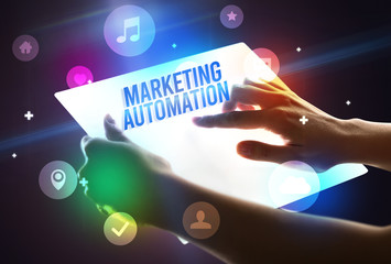 Holding futuristic tablet with MARKETING AUTOMATION inscription, new technology concept