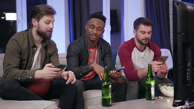 Portrait of attantive likable 30s diverse guys which get distracted on their phones during watching sport game on tv