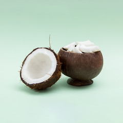 Half of coconut and coconut pieces in wooden vase on mint background.
