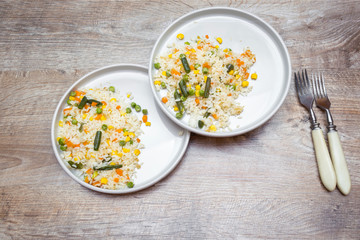 risotto with vegetables served on two white plates with forks. rustic food wooden background. minimal style, top view.