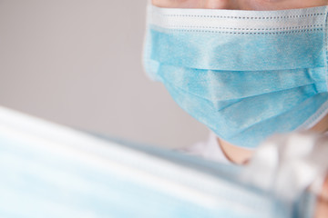Person wearing blue medical mask and white shirt holding some medical masks meant to prevent corona...