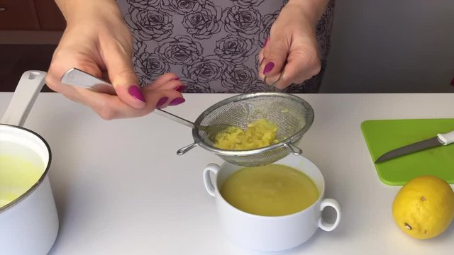 A girl passes cooked lemon Kurd through a sieve and separates the zest. Ready lemon kurd is poured into containers and decorated with fresh lemons.
