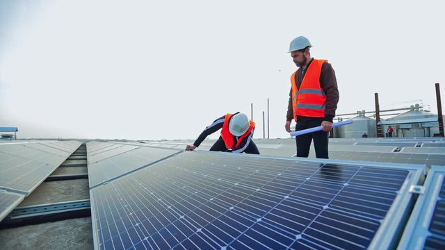 Sustainable green energy installation. Technicians in orange uniform and hardhats working with solar panels on the energy farm.