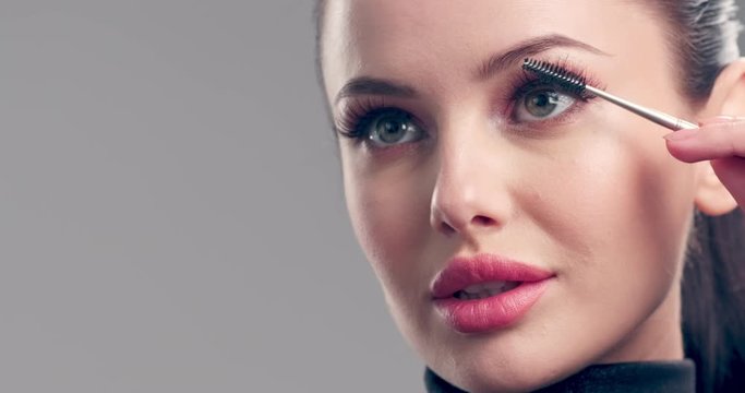 Woman makes makeup. Young woman paints her eyelashes with an eyelash brush.  Cosmetic concept. Beautiful brunette model doing make-up. 4k Slow motion footage. Closeup view.
