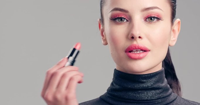 Young woman paints her lips with lipstick. Beautiful brunette model doing make-up. Woman makes makeup before camera.  Cosmetic concept. 4k Slow motion footage. Closeup view.
