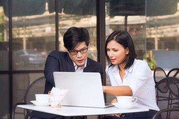 Obraz premium Co working space concept. Asian business looking and thinking in front of laptop while sitting at co-working space. young women and man working of new ideas in coffee shop.