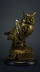 beautiful statuette of gold color figure of an owl with a feather on books on a black background