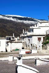 View over town rooftops towards the snow capped mountains of the Sierra Nevada, Pampaneira, Spain.