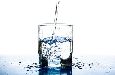 A stream of water pours into a glass on a white background. Water drops on the table.