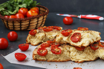 Pieces of focaccia with cherry tomatoes are located on parchment on a dark background