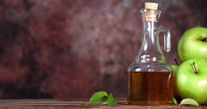 Apple cider vinegar is rotating on a wooden table.