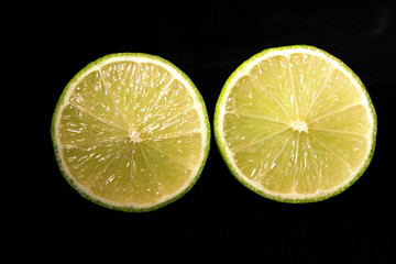 Lime slices isolated on black background. Two green fresh limes cut in half close-up. Design element