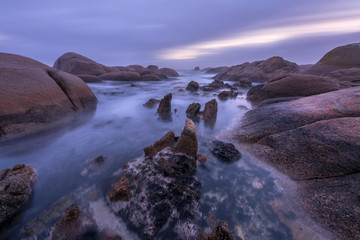 A beautiful misty long exposure seascape taken before sunrise, with clouds in the dramatic sky and large rocks in the foreground, taken at Paternoster, South Africa.