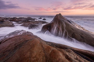 A beautiful misty seascape after sunset with clouds in the sky, with the waves splashing over the large rocks in the foreground, taken at Paternoster, South Africa.